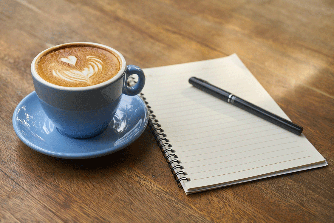 A cup of coffee with a notebook and pen