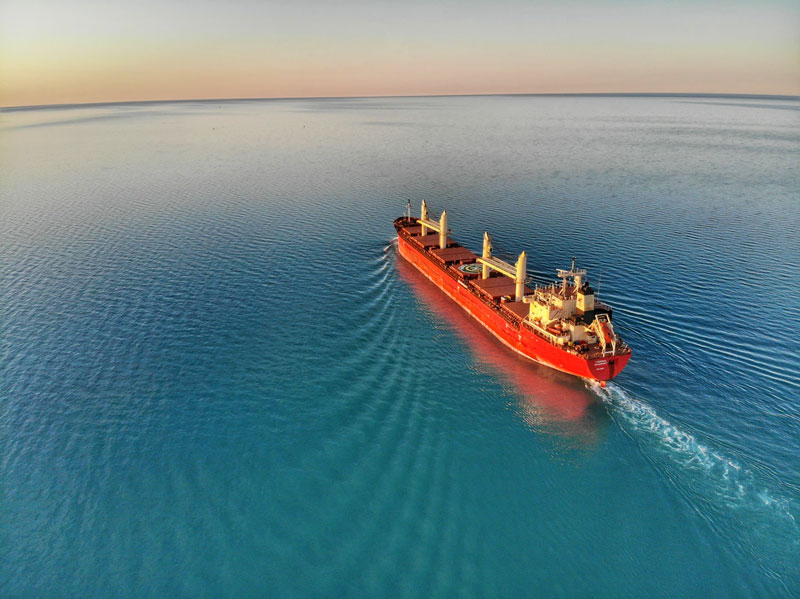 A red shipping carrier sails through bright blue water.