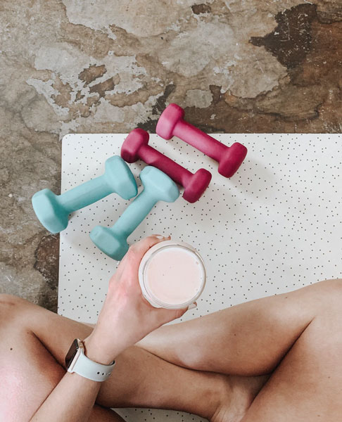 A woman sits on her yoga mat while holding a weight loss smoothie with hemp oil