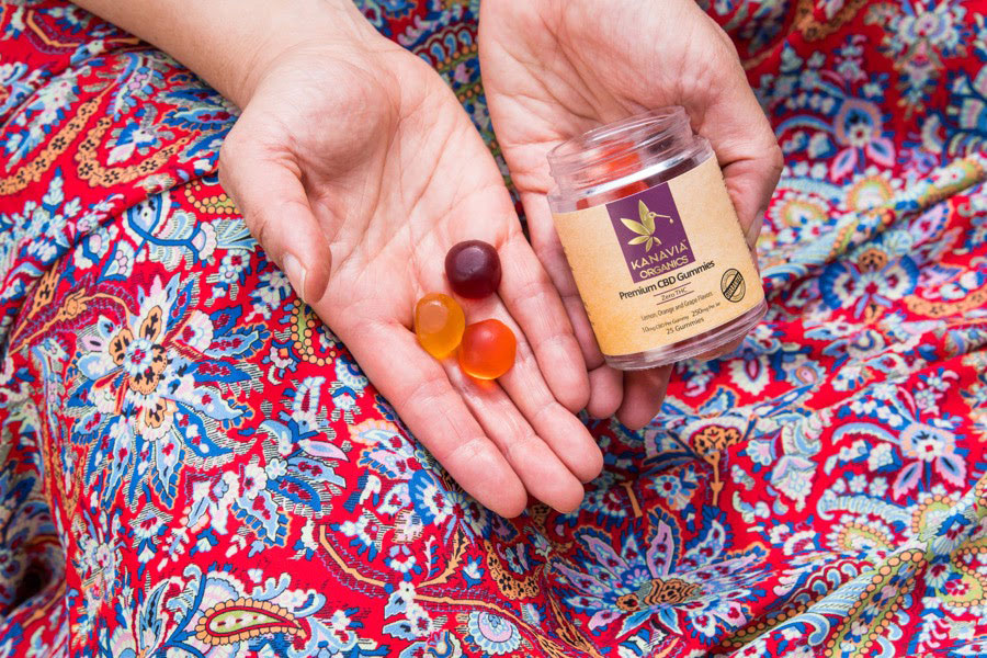 woman in red dress holding Kanavia Organics CBD gummies, including product tub