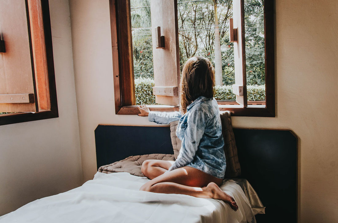 A woman stuck at home looks out her bedroom window.