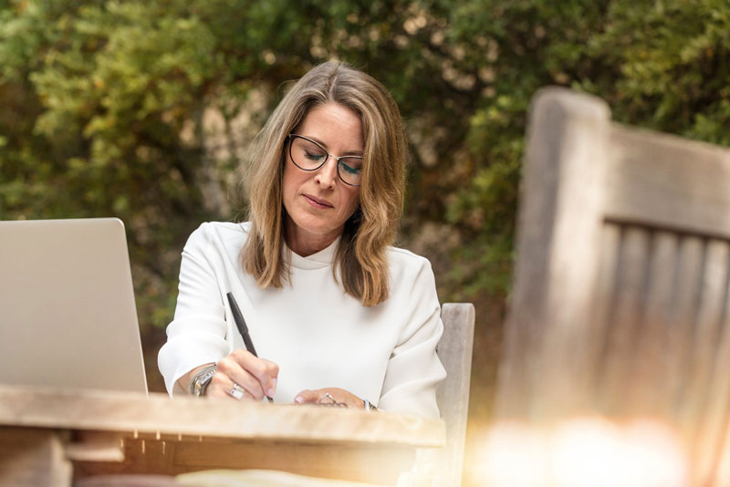 A woman sits at an outdoor table and takes notes on CBD for menopause