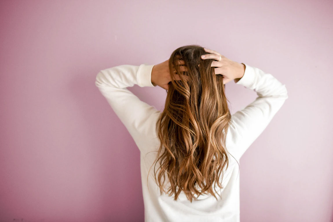 A woman stands and holds her head against a pink background.