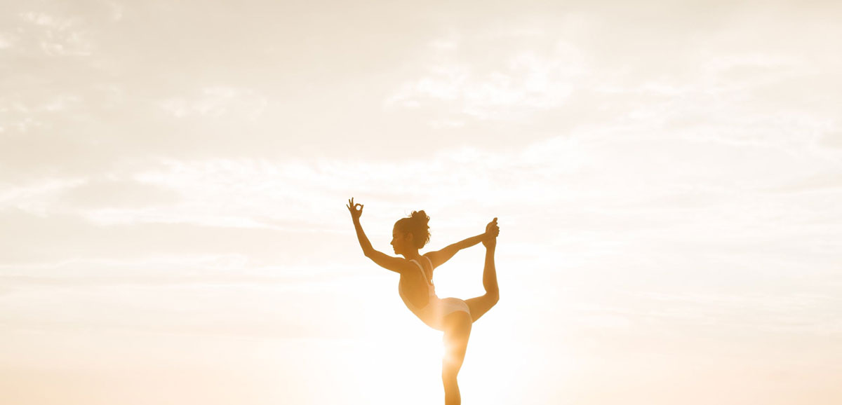 A woman holding a yoga pose in front of the setting sun